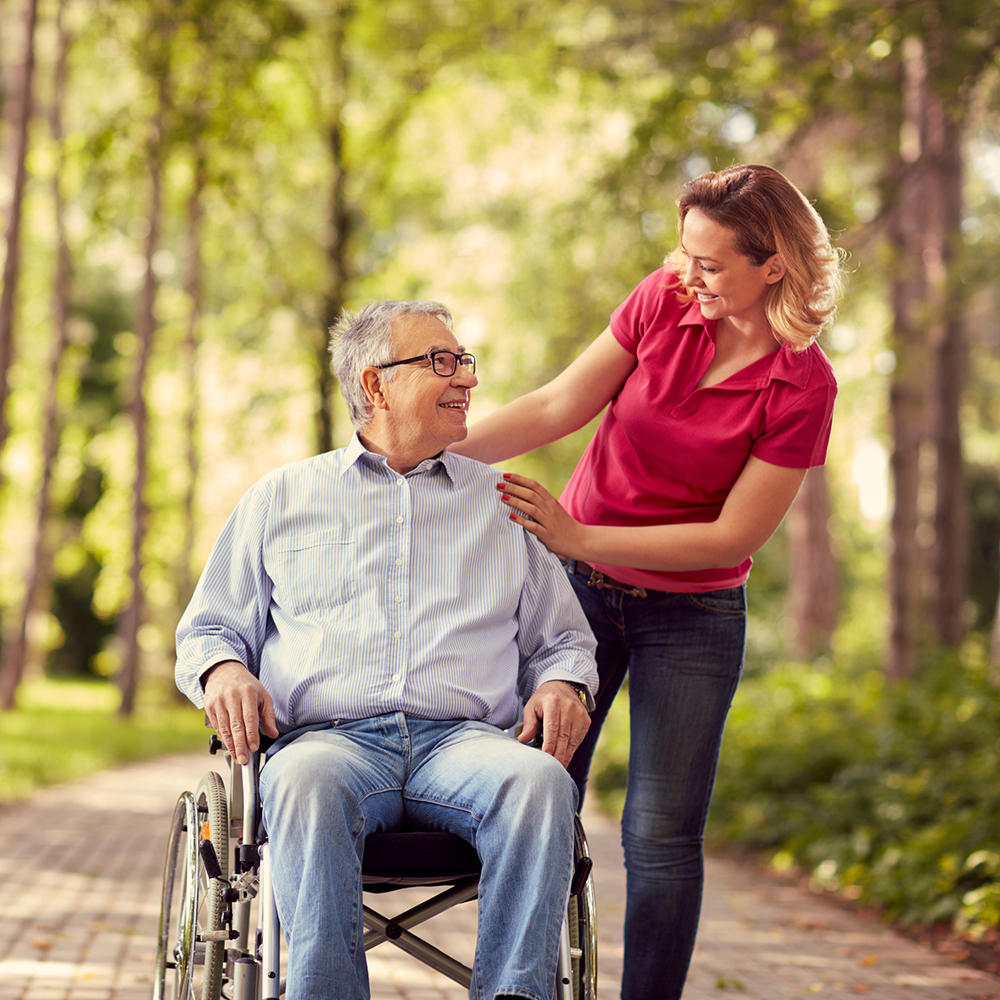 Young woman standing next to an elderly man in a wheelchair outside; Beaver Dam Community Hospital hospice volunteer